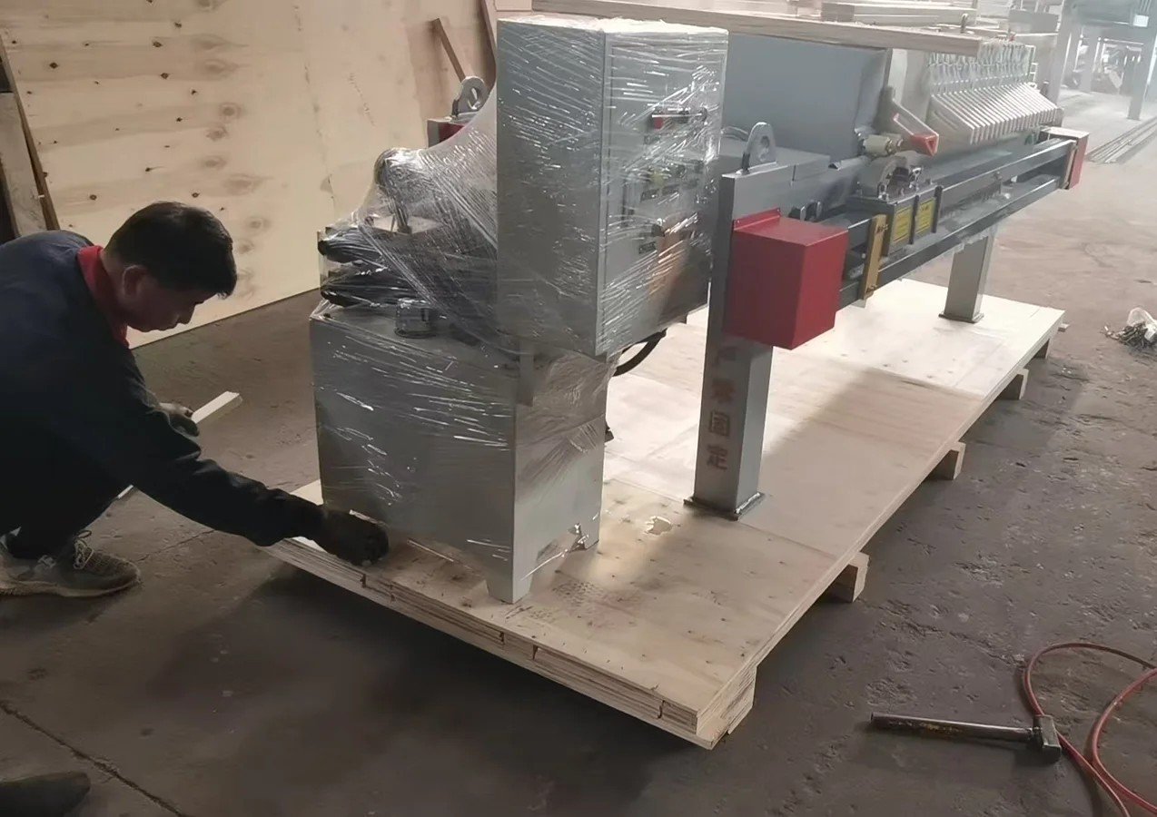 Worker wrapping a finished Loway filter press in export-grade protective film before the crate closes