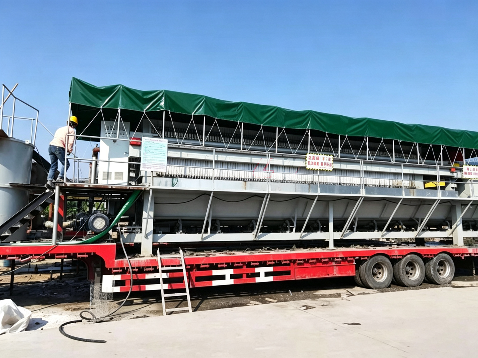 Loway mobile filter press transported on a flatbed truck for wastewater treatment with green weather canopy