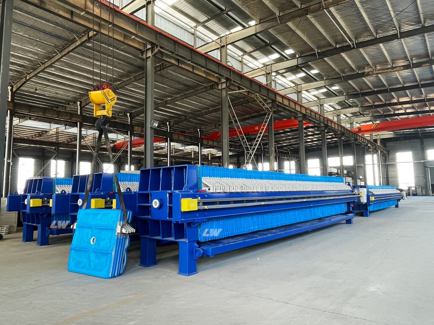 Crane lifting a filter plate pack during assembly at the Loway factory